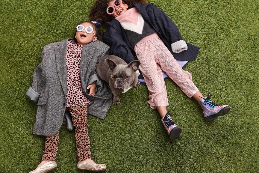 Kids with sunglasses laying on the lawn with a french bulldog.